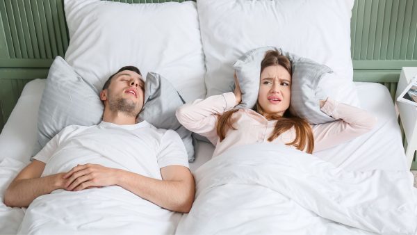 Husband snoring in bed, wife covering her ears with a pillow | SleepTest.co.uk